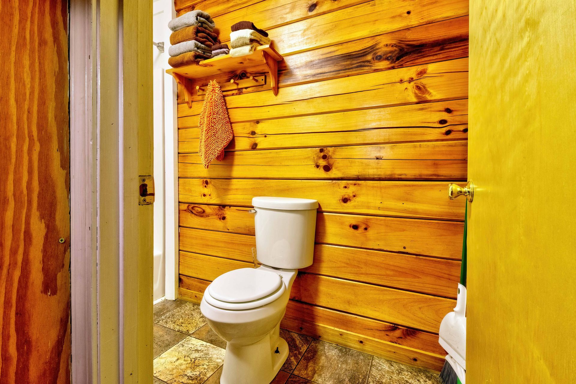 Rustic bathroom with a white toilet, wooden plank wall, and yellow-painted doorway.