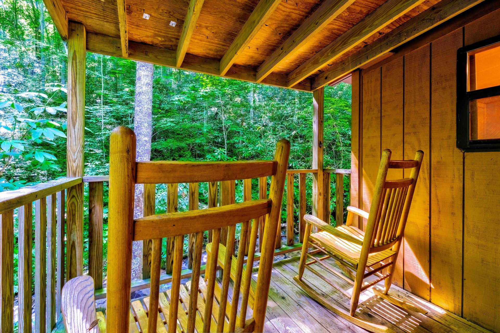 Wooden cabin porch with rocking chairs overlooking a lush green forest