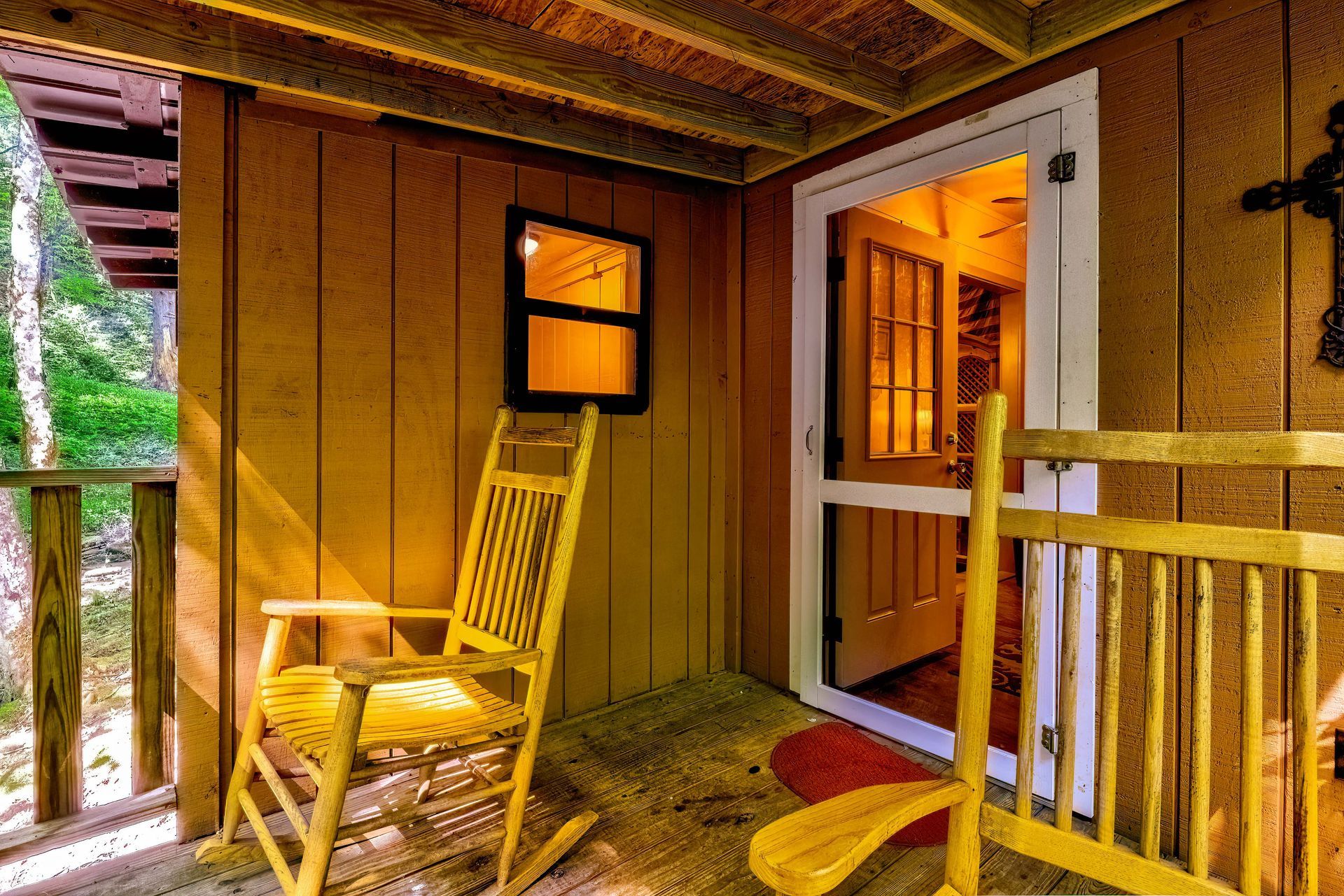 Wooden porch with a rocking chair, open door, and warm light spilling from inside