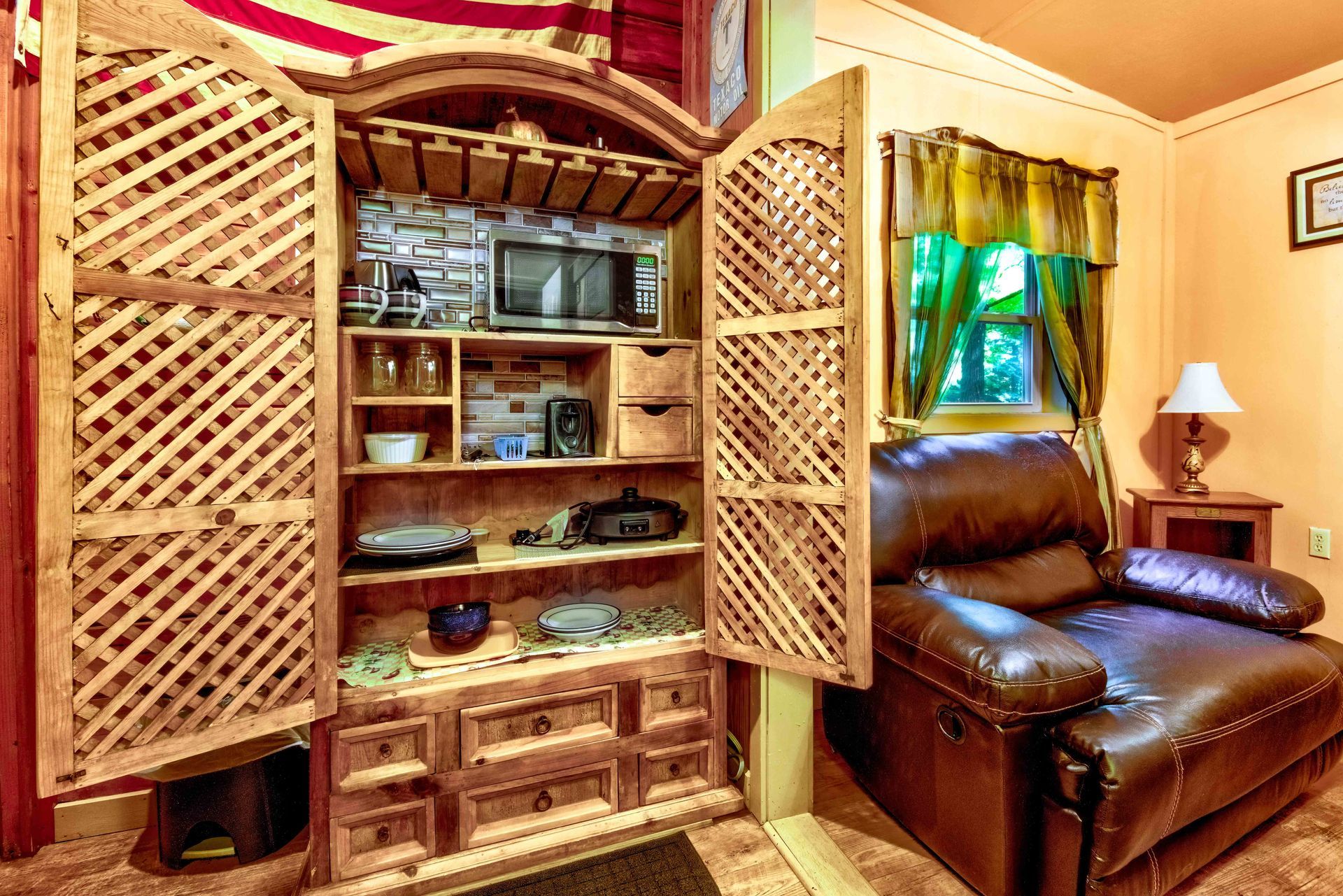 Wooden hutch cabinet with lattice doors in a cozy living room beside a brown leather sofa and window.