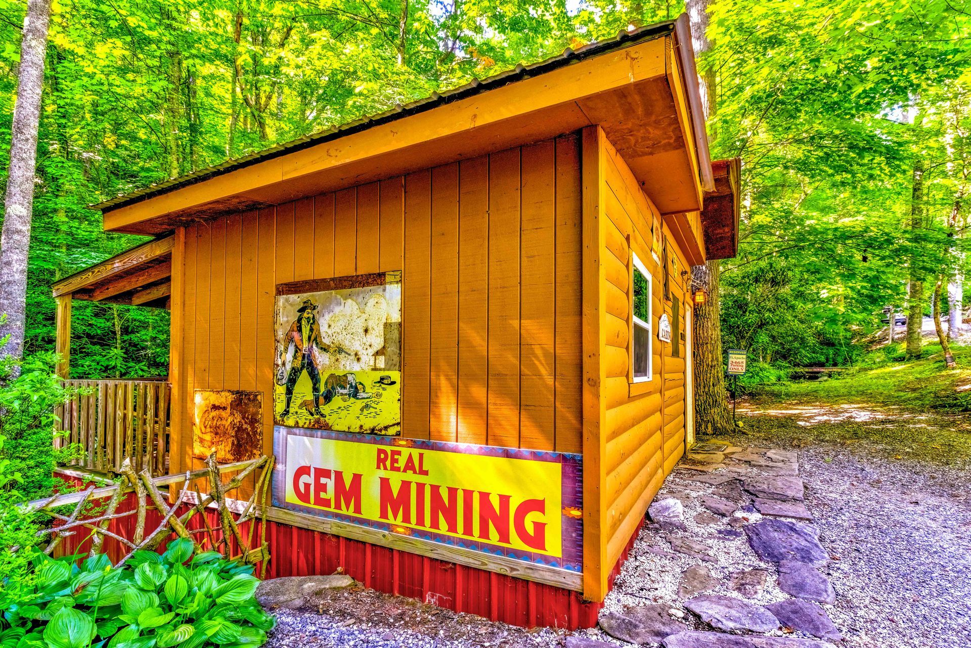 Small wooden cabin with a “Real Gem Mining” sign in a bright green wooded setting