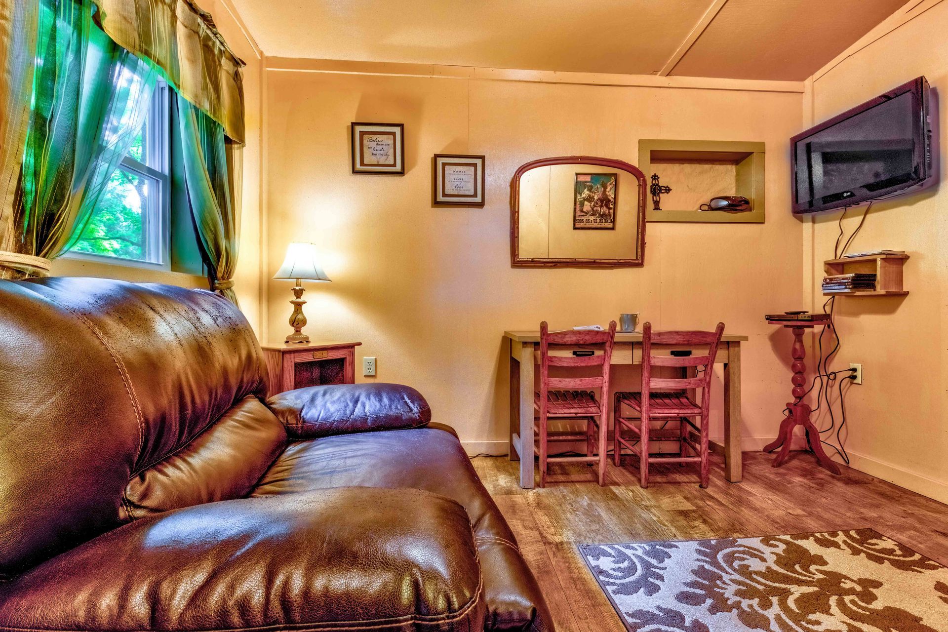 Cozy living room with brown leather sofa, small dining table, wall-mounted TV, and patterned rug