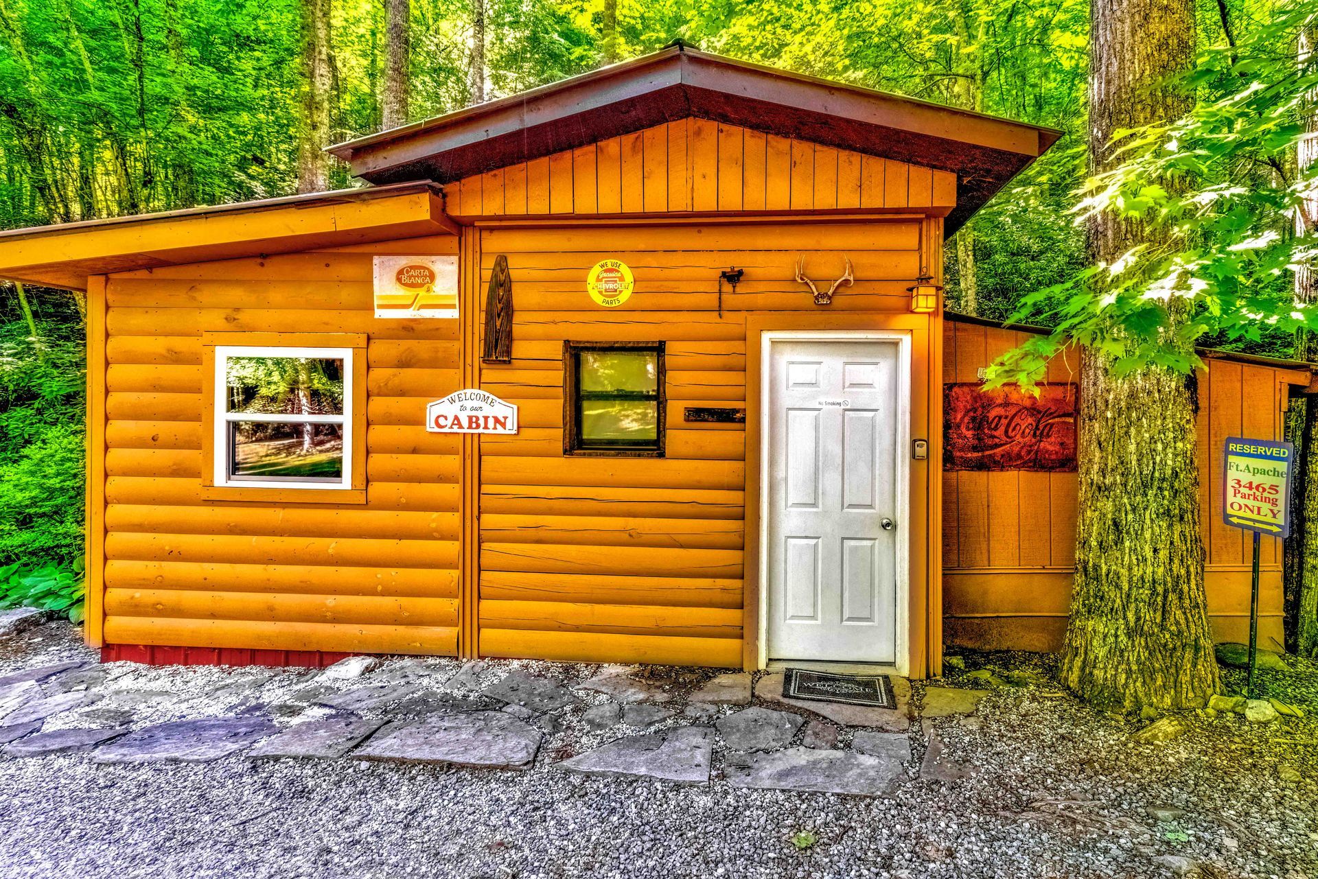 Small orange log cabin in a wooded area with a white door and rocky ground in front