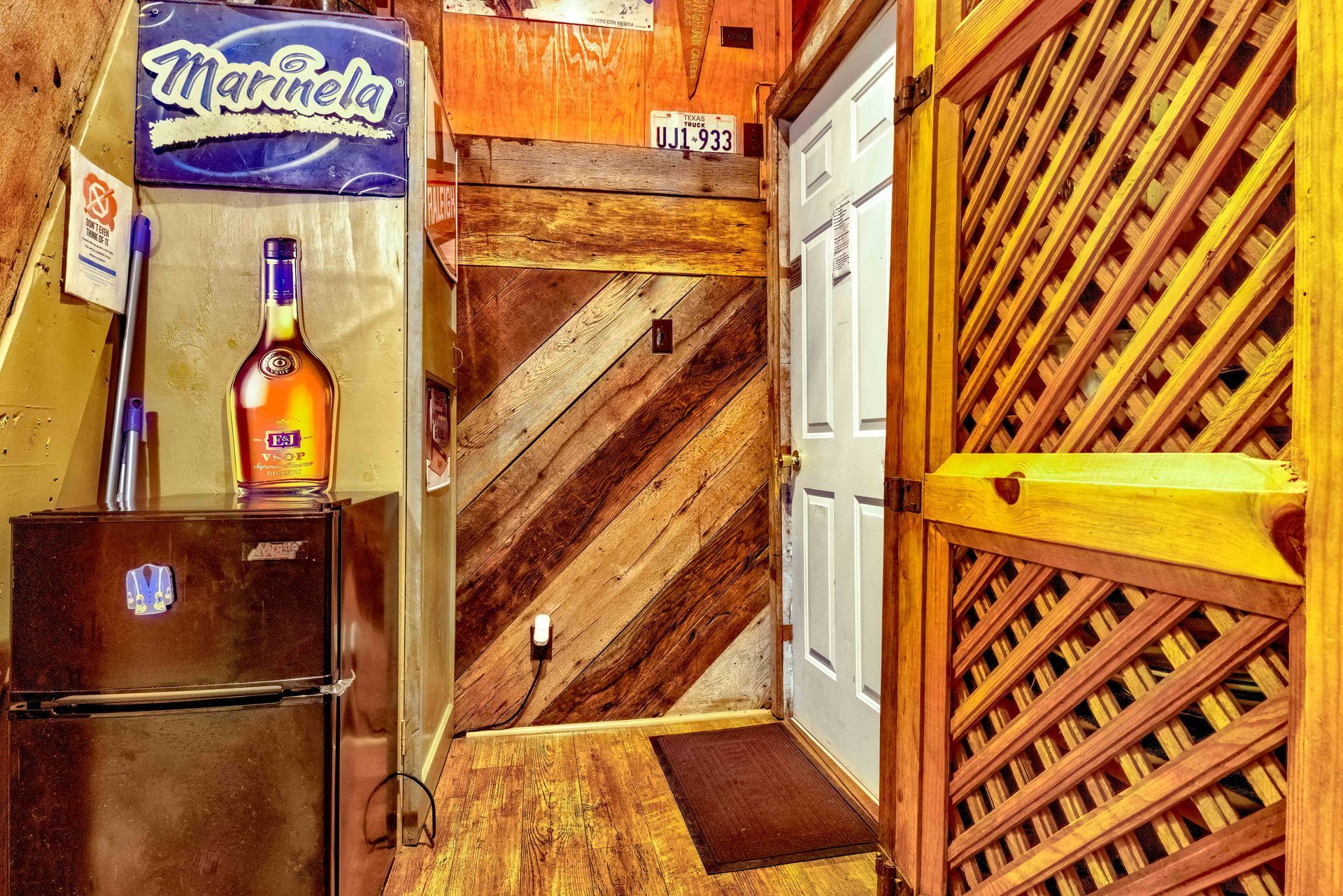 Warm-toned rustic hallway with wooden doors, lattice wall, small refrigerator, and a bottle display