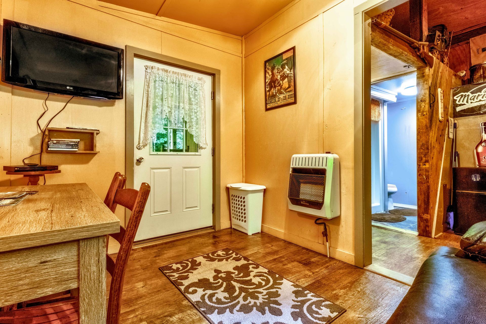 Cozy rustic room with TV, desk, door, small heater, and rug leading to hallway