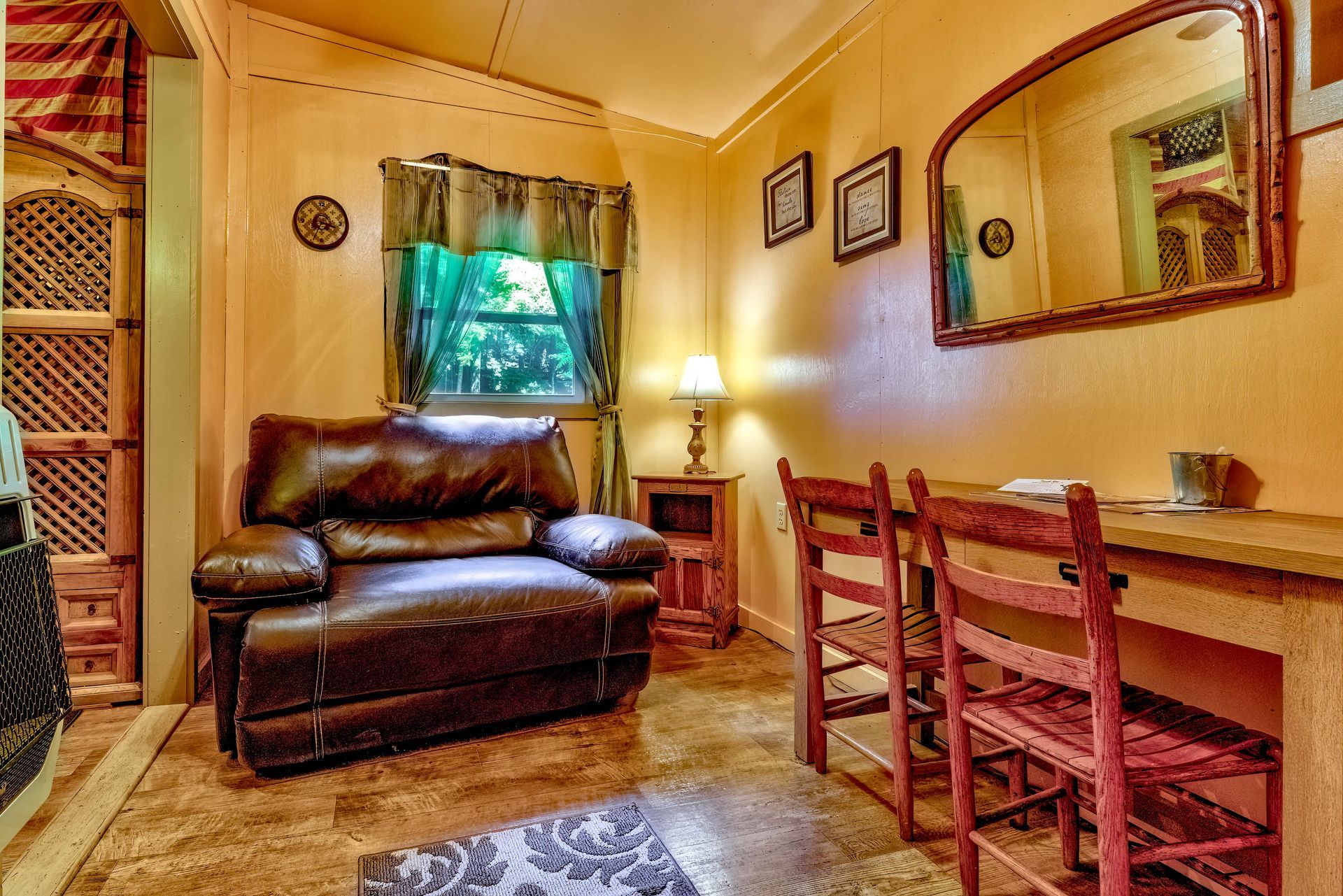 Cozy living room with leather recliner, wooden desk and chairs, lamp, wall mirror, and window with curtain.