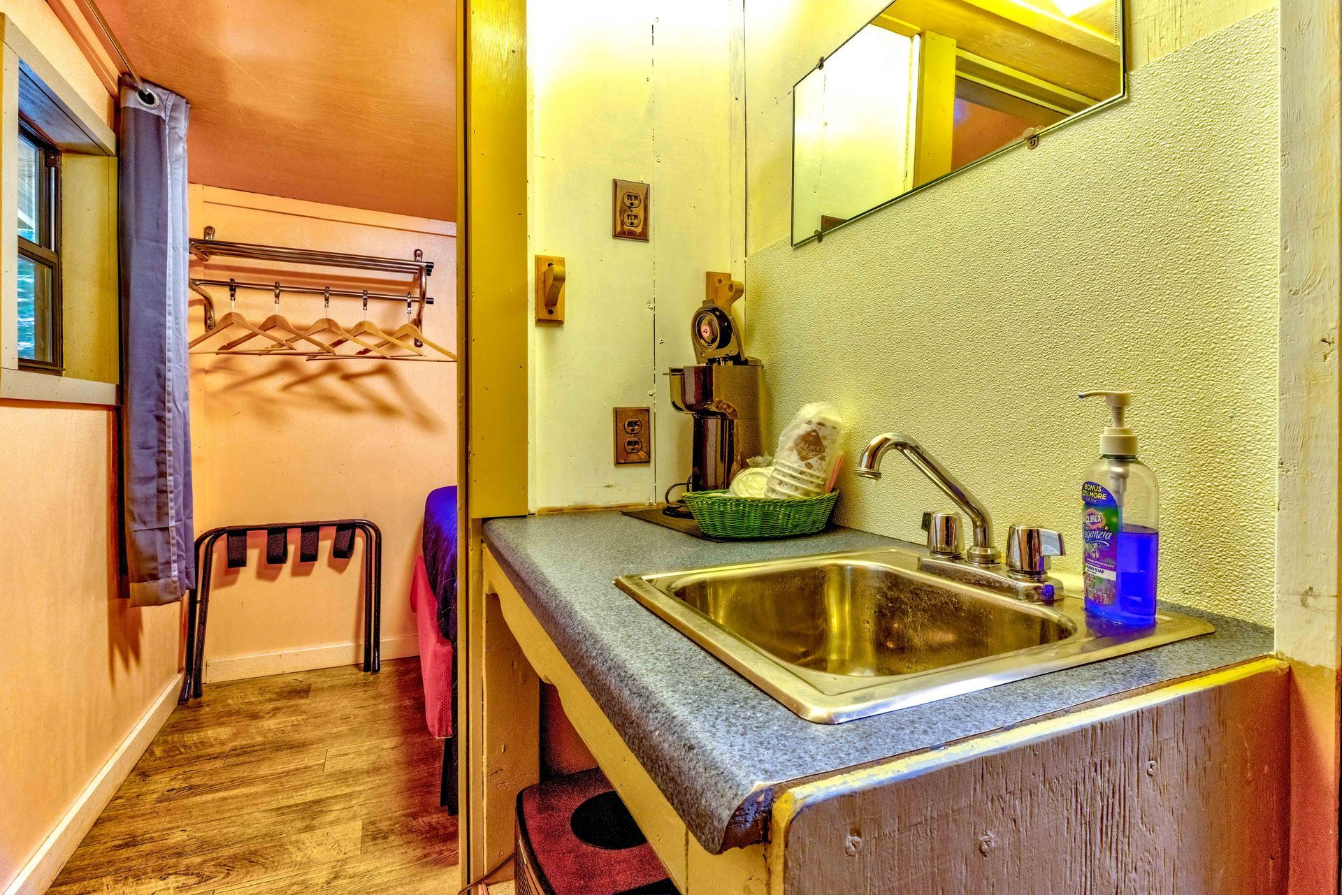 Narrow hallway with a sink counter, mirror, and wall hooks in a small apartment entryway.