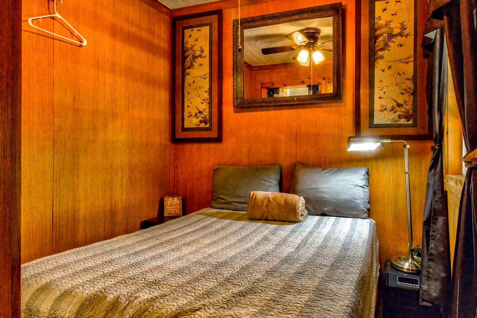 Cozy wood-paneled bedroom with a bed, lamp, framed artwork, and mirror on the wall
