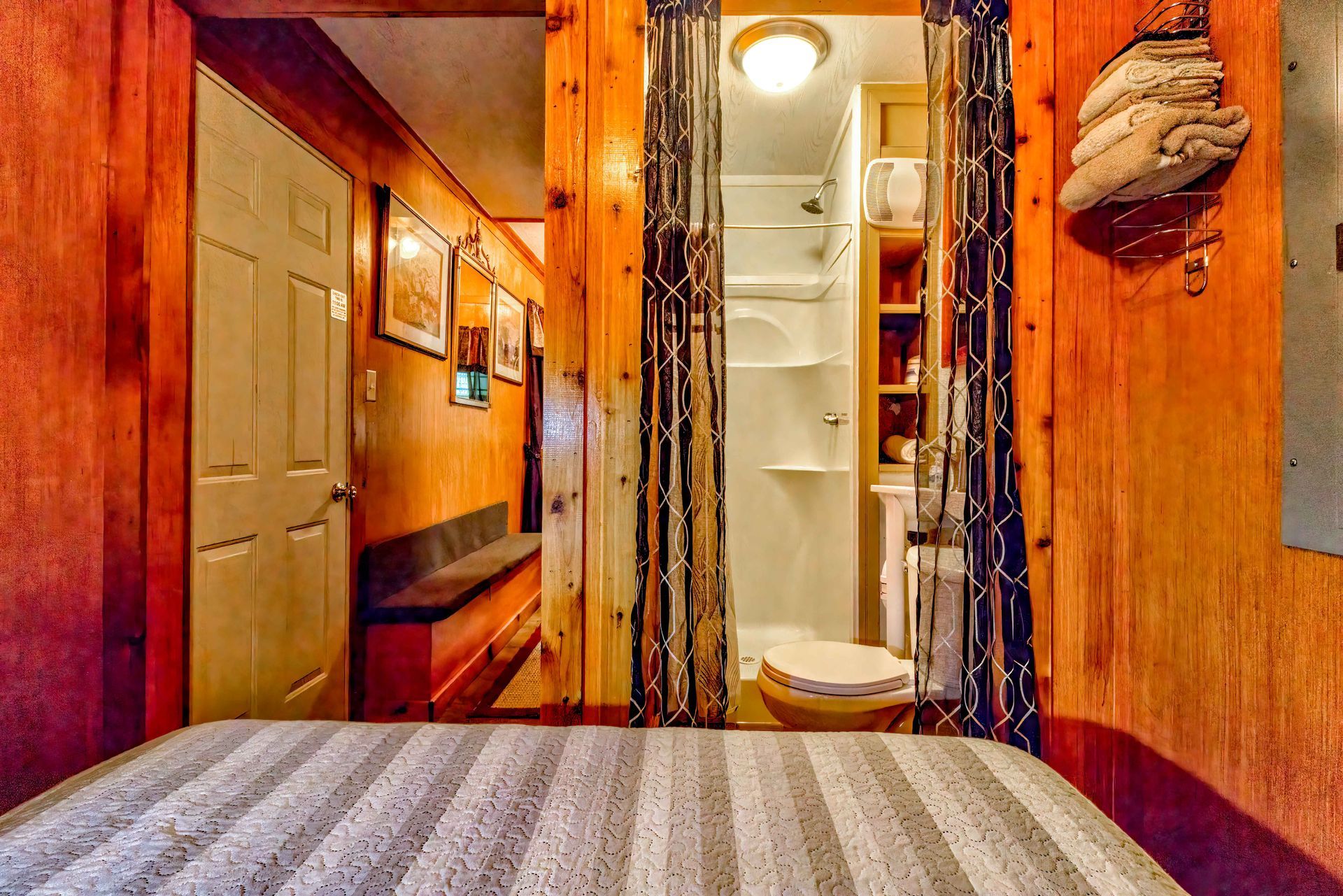 Narrow cabin hallway with wood paneling, leading to a small bathroom with a toilet and shower.