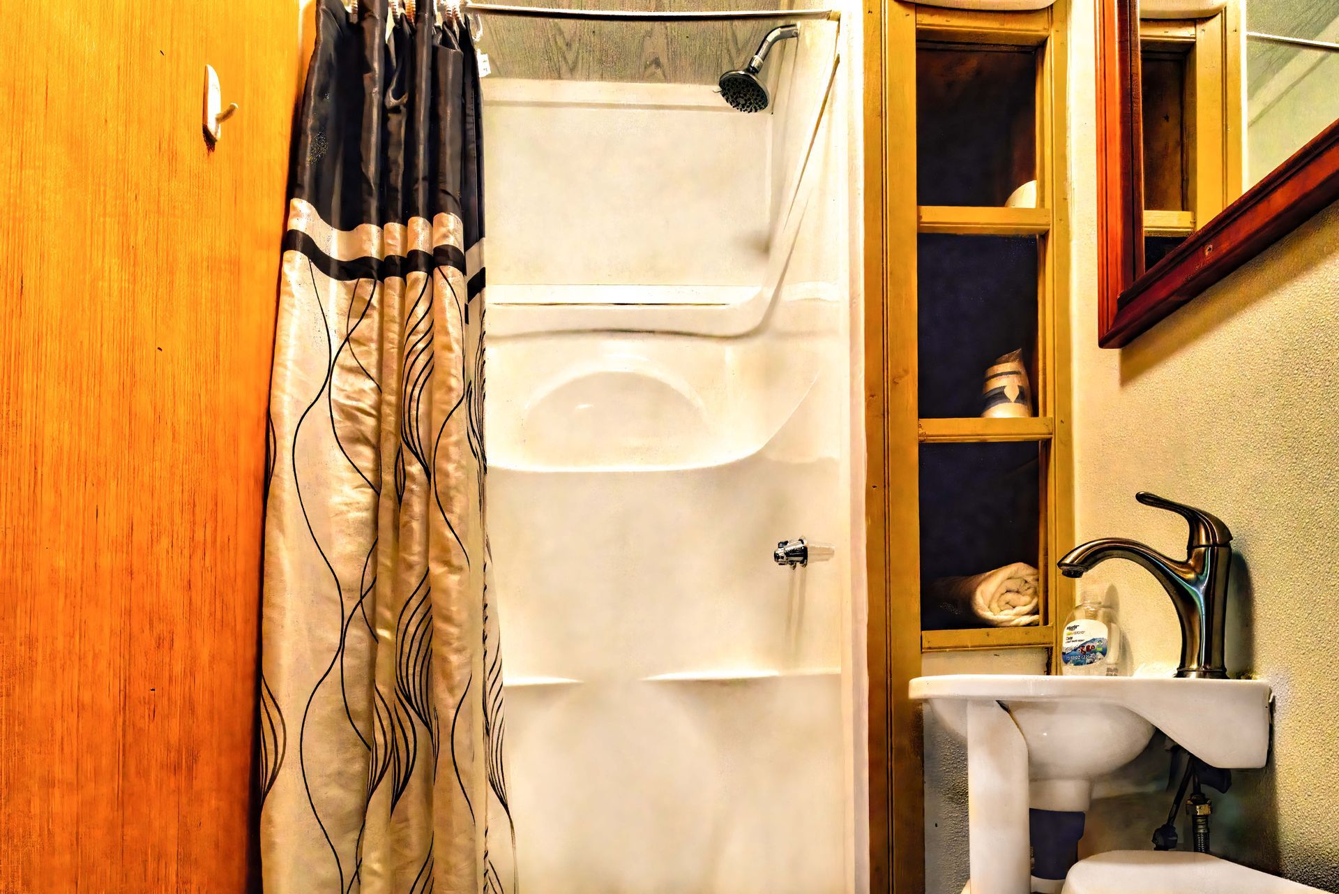 Small bathroom with shower curtain, bathtub, sink, and wooden storage shelves.