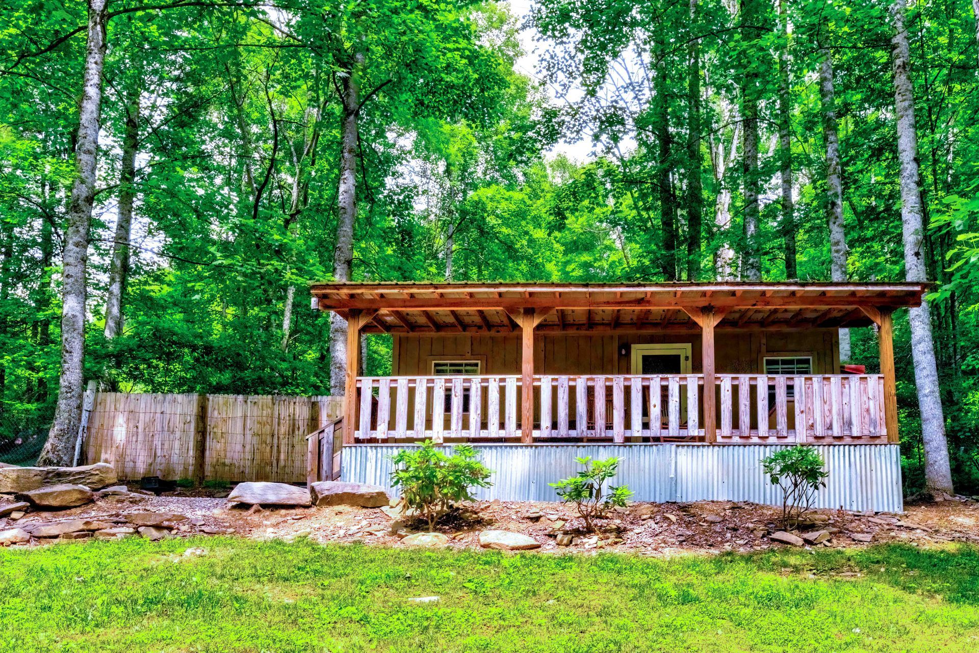 Small rustic cabin with a porch in a green wooded yard