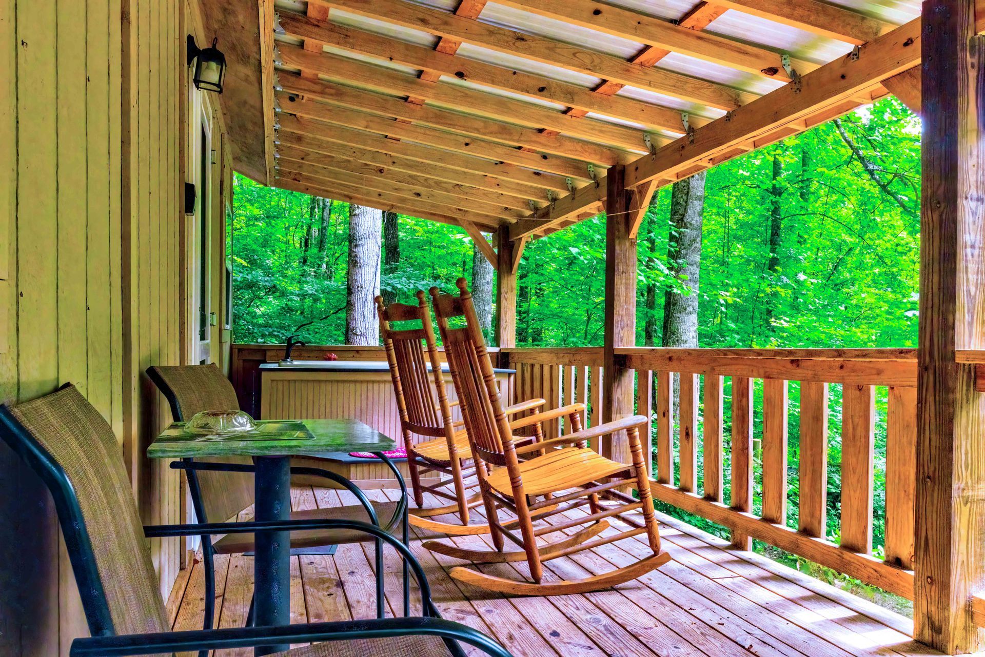 Covered wooden porch with rocking chairs overlooking a lush green forest