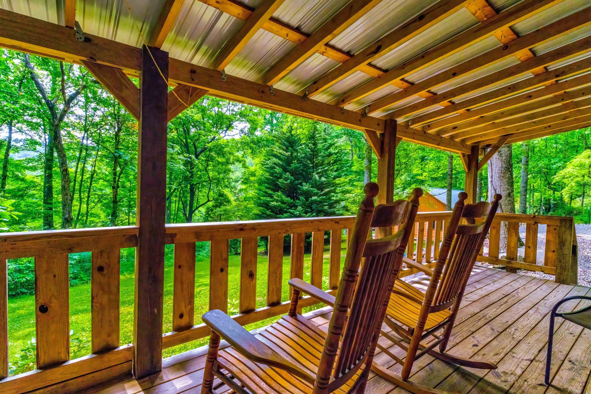 Covered wooden porch with rocking chairs overlooking a green wooded yard