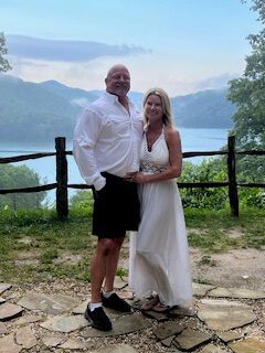 Couple posing on a stone path with a lake and mountains in the background, both in white and black attire