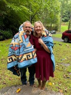 Smiling couple standing outdoors in a lush garden, wrapped in colorful blankets on a rainy day