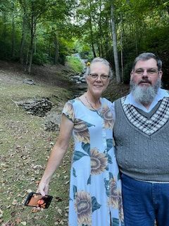 Two people standing on a forest trail, smiling at the camera.