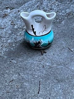 Small painted ceramic vase with a white top and blue-black base on a concrete surface.