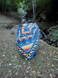 Person covered in a bright patterned blanket walking through a wooded streambed