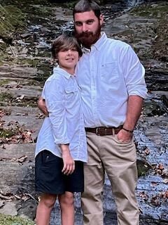 Two people standing together on rocks beside a stream, wearing white shirts and smiling.