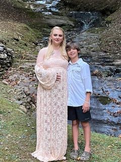 Woman and boy standing by a small waterfall on a rocky forest trail, both smiling.