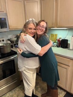 Two people hugging in a kitchen, smiling beside a stove and countertop.