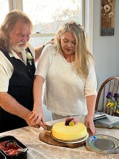 Couple cutting a yellow frosted cake on a table at a home celebration