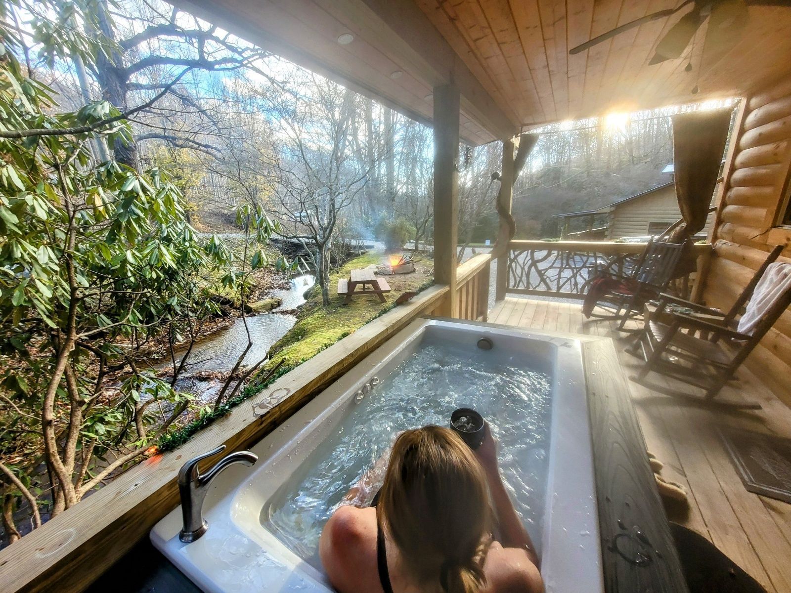 Person relaxing in a hot tub on a covered porch overlooking a wooded yard