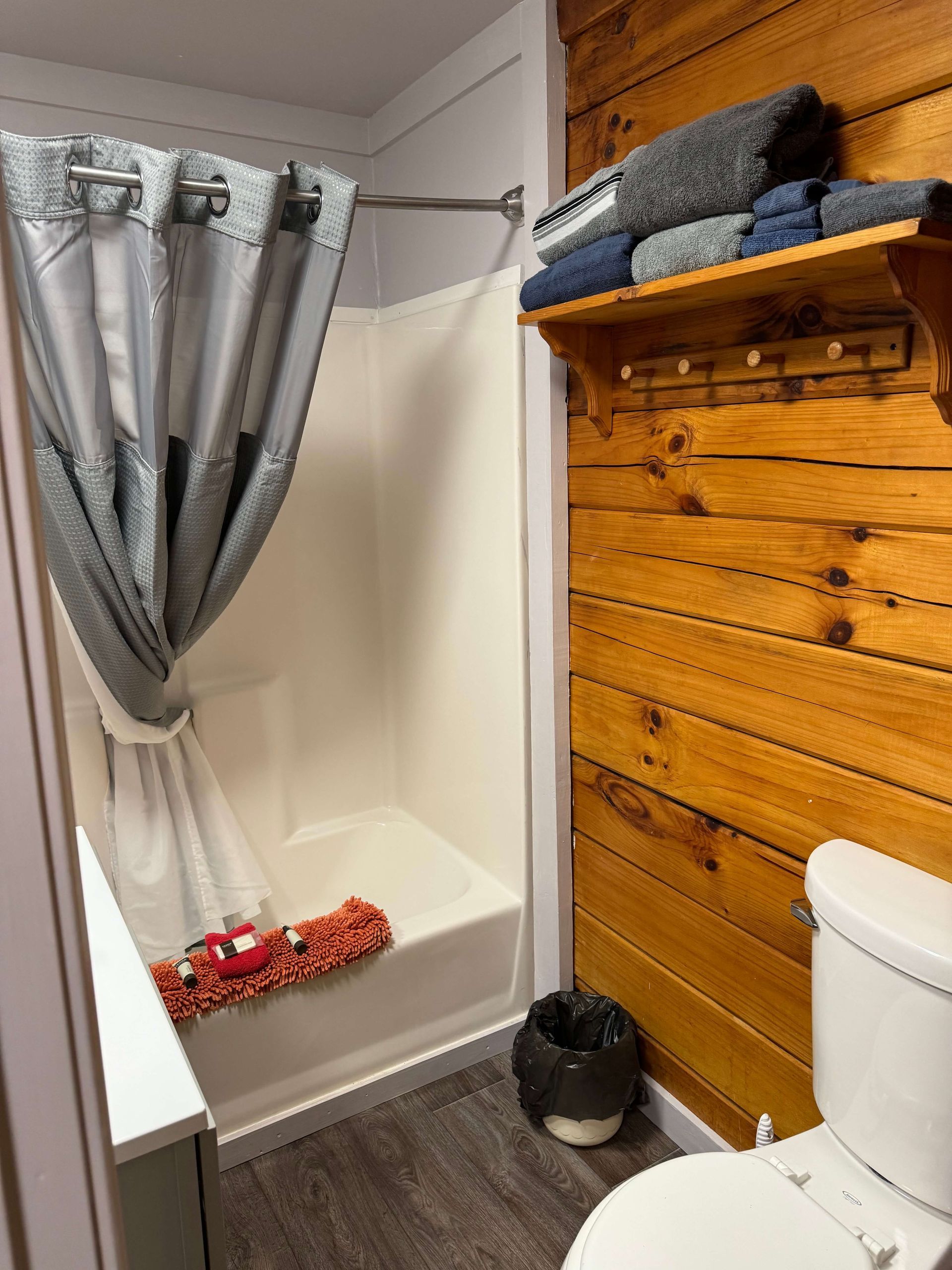 Small bathroom with a shower curtain, wood wall, folded towels, and a toilet beside the shower stall