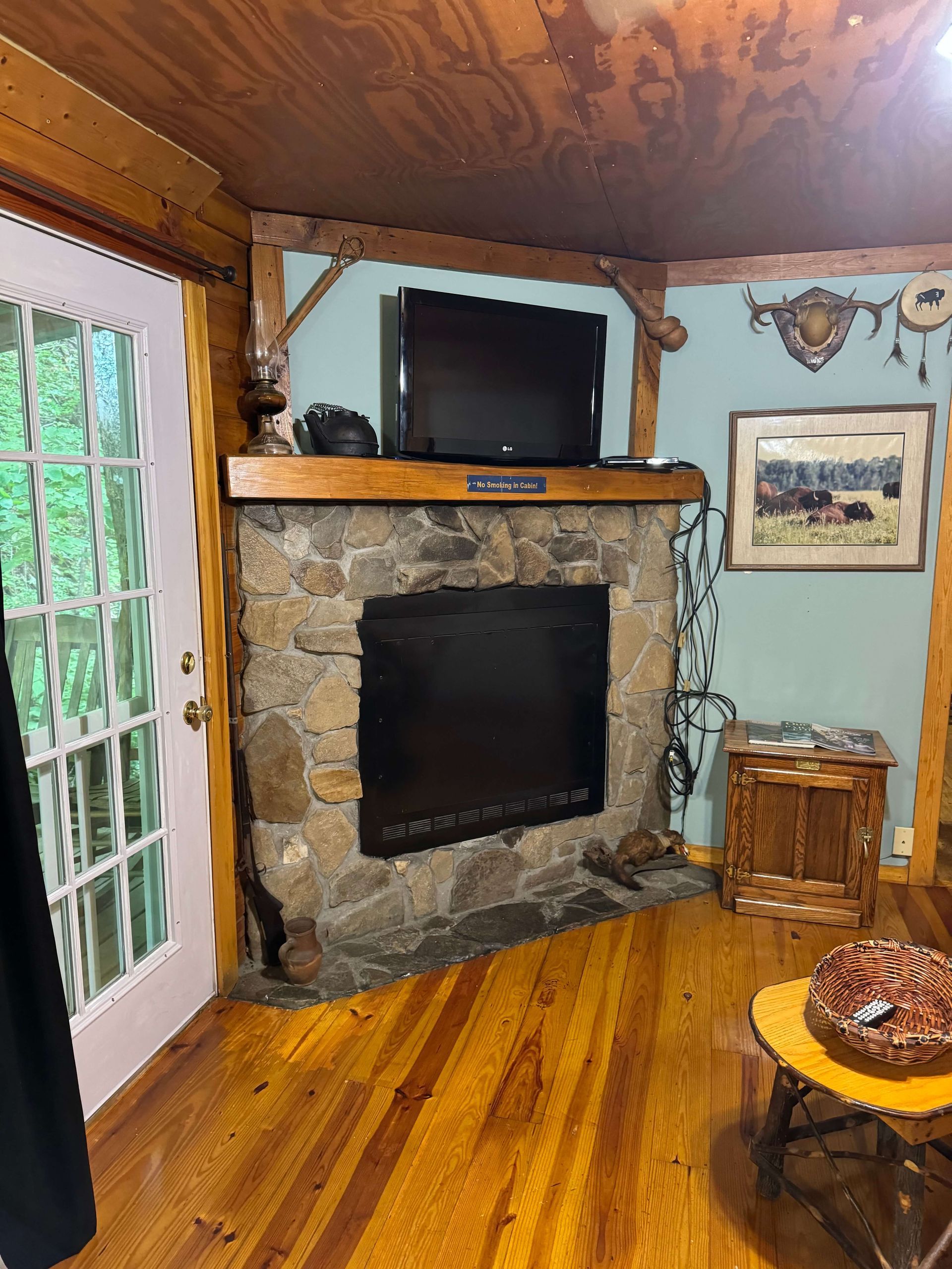 Cozy rustic living room corner with stone fireplace, wood-paneled walls, TV, and French doors