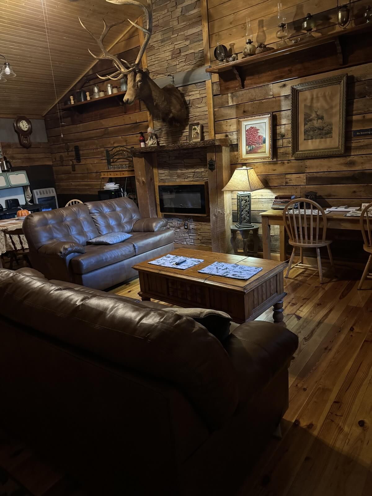 Rustic lodge living room with leather sofas, stone fireplace, mounted antlers, and warm wood decor.