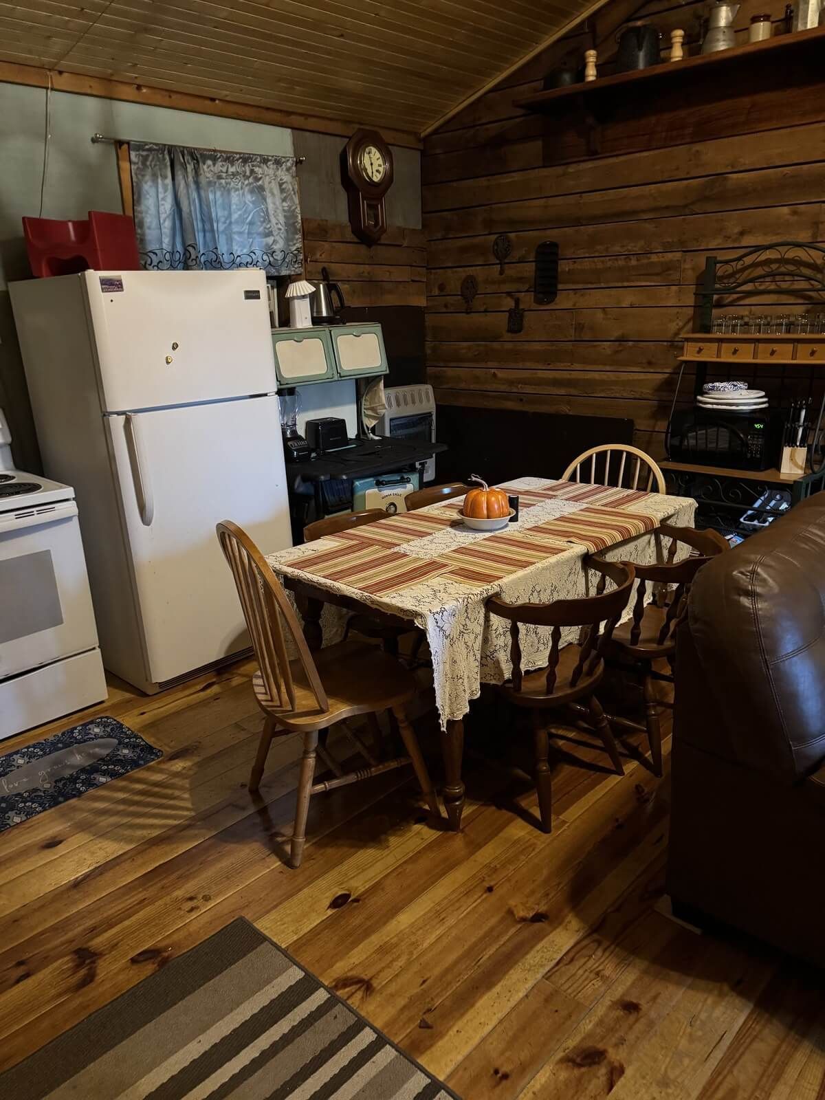 Rustic kitchen with wooden walls, white fridge, dining table, and chairs under warm lighting