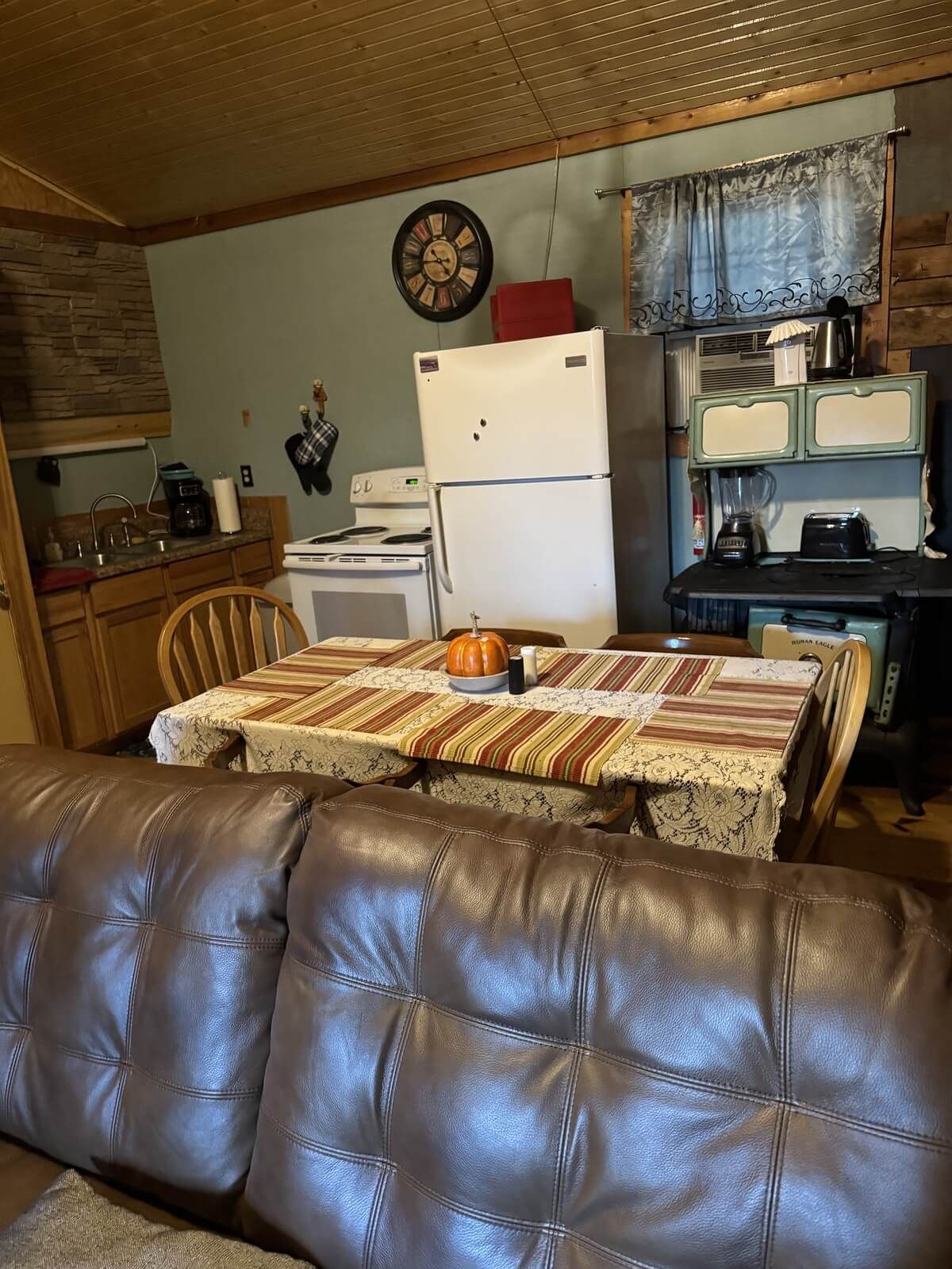 Cozy kitchen and dining area with white fridge, wooden table, and brown leather couch in foreground