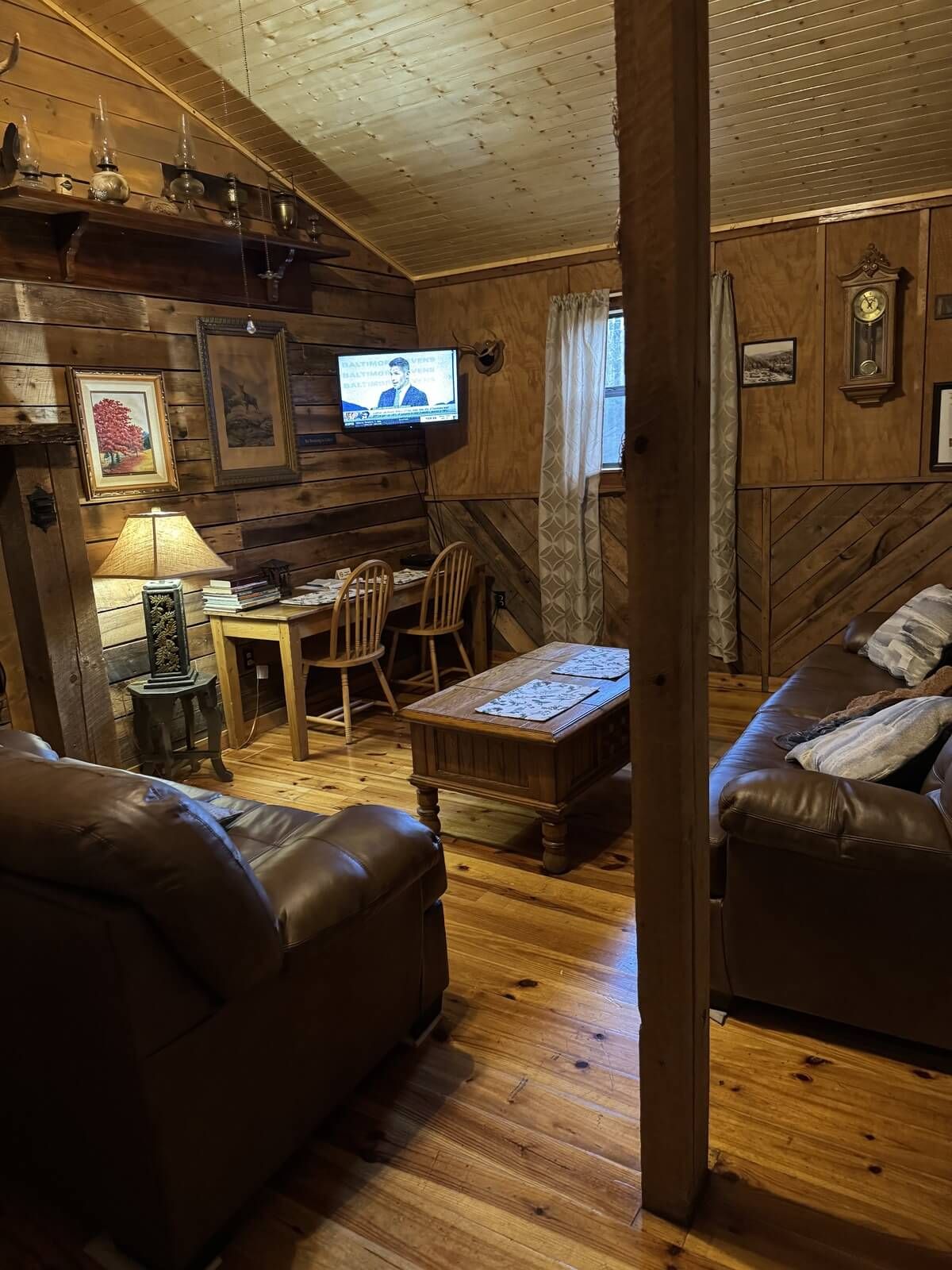 Cozy wood-paneled cabin living room with leather chairs, TV, desk, and rustic decor