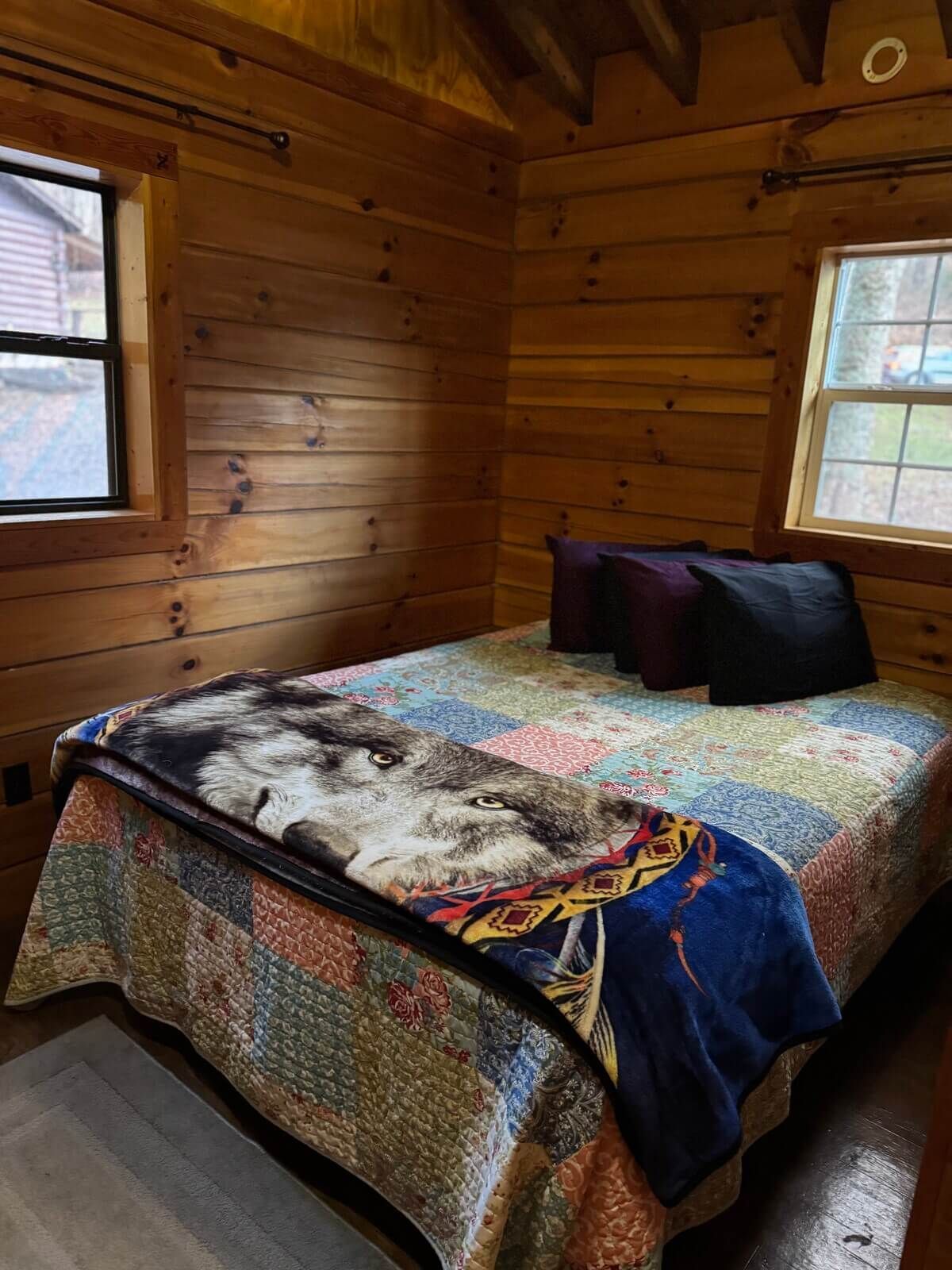 Cozy log cabin bedroom with a made bed, patterned quilt, and two pillows by a window.