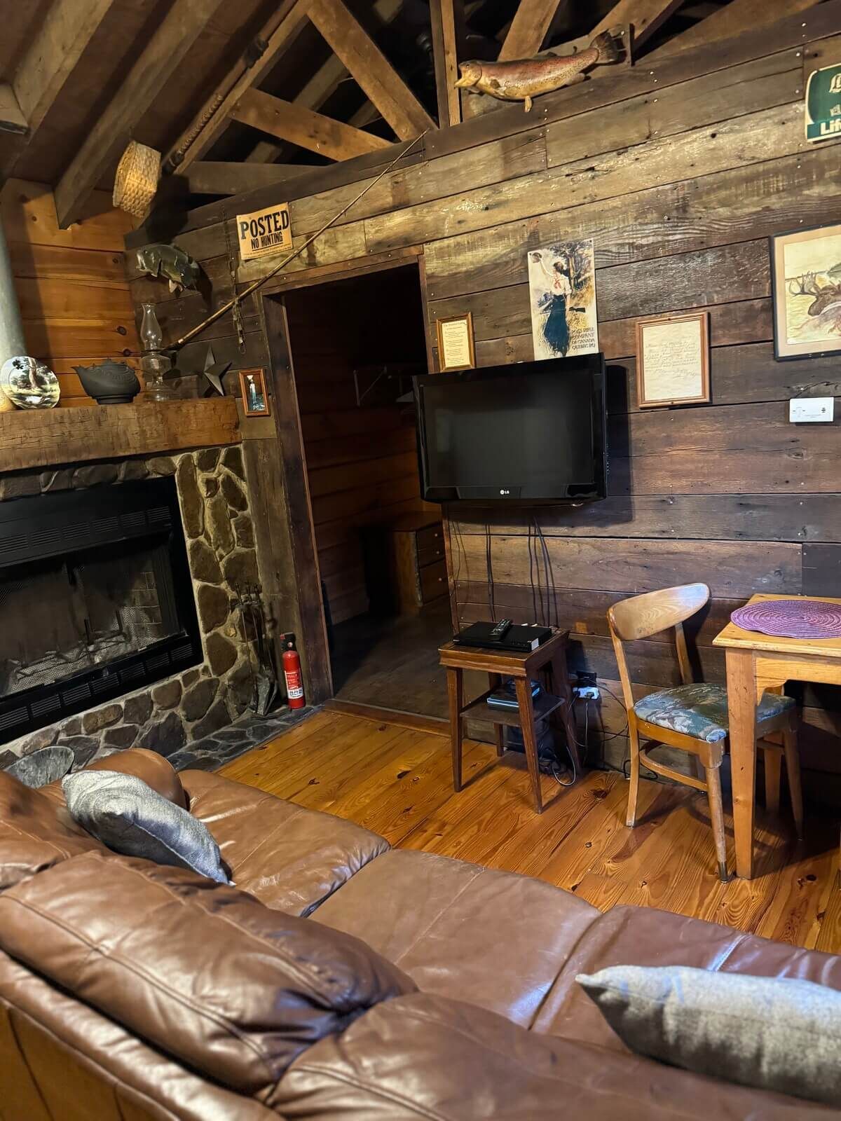 Rustic lodge living room with stone fireplace, TV, leather sofa, and wooden table under exposed beams