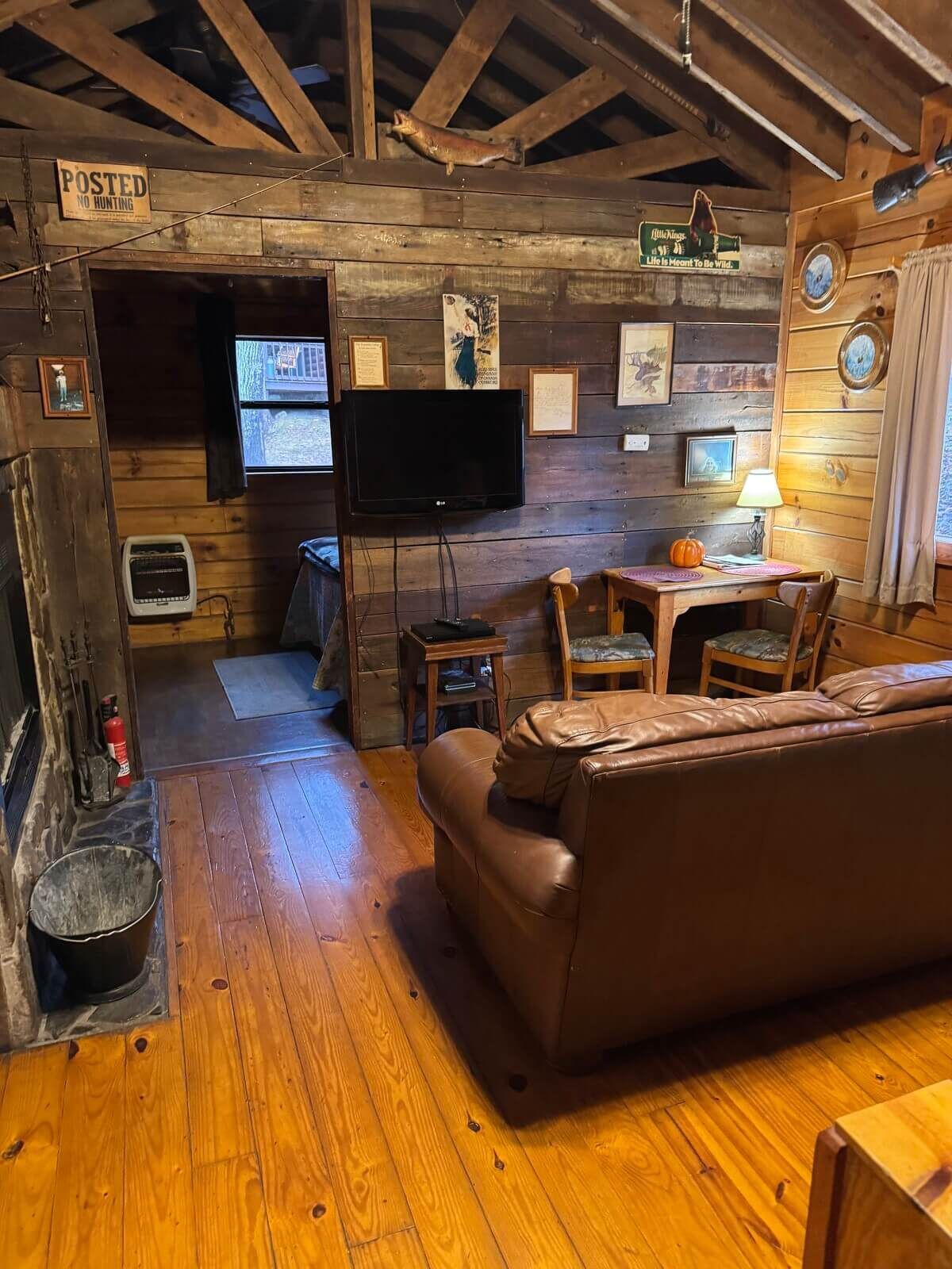 Rustic cabin living room with wood beams, leather couch, TV, desk, and warm wooden floors