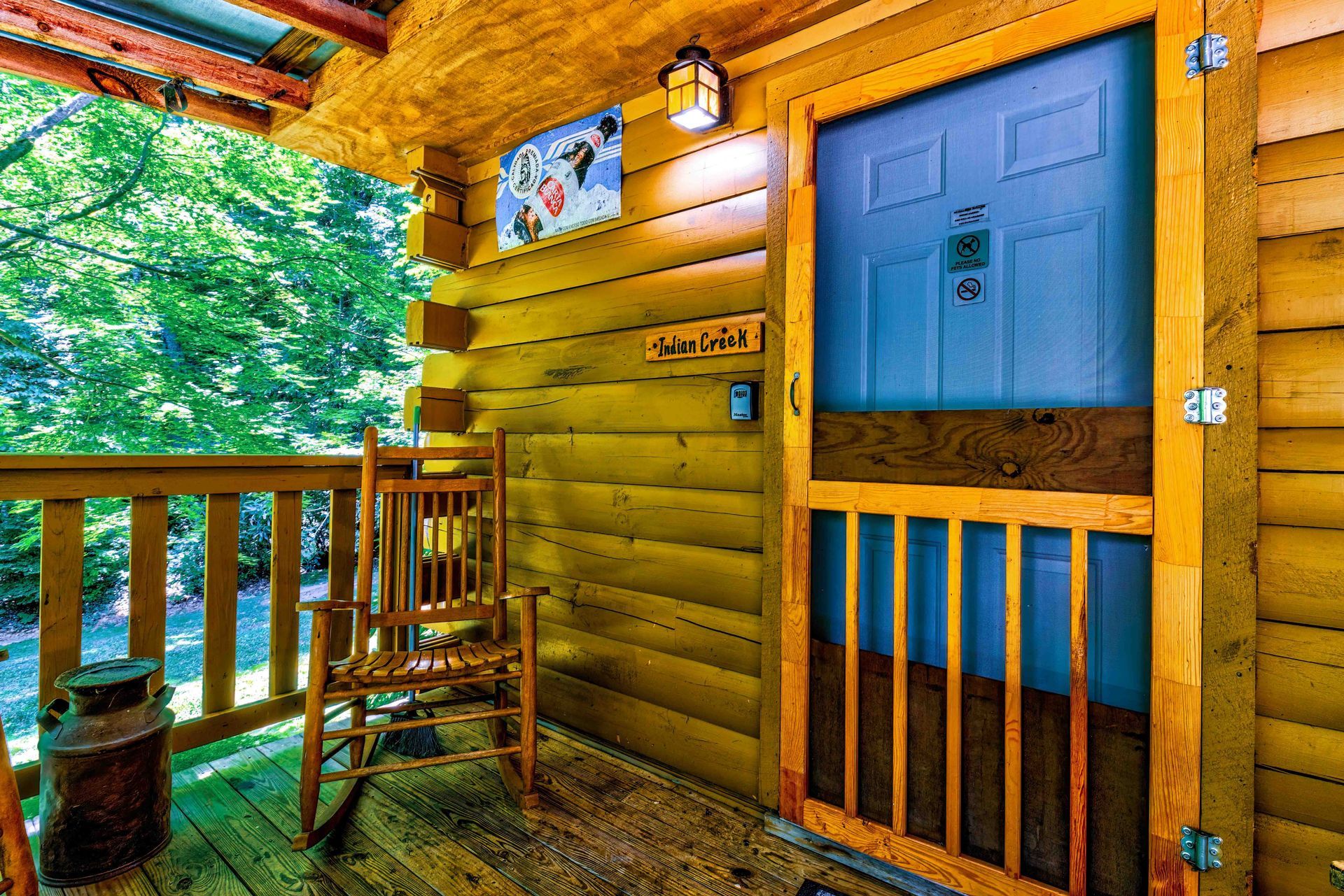 Wooden cabin porch with chair, railing, and a blue door overlooking green trees