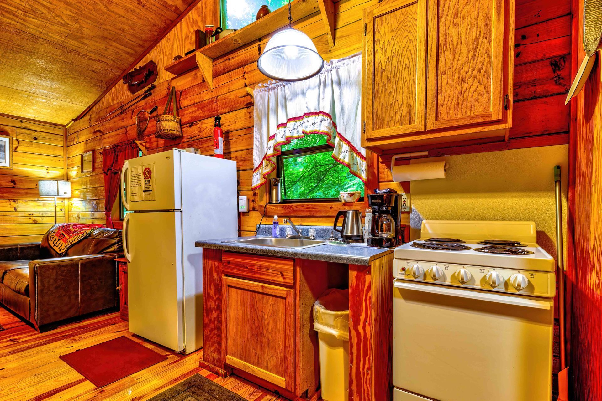 Cozy cabin kitchen with wood-paneled walls, white refrigerator, stove, sink, and wooden cabinets.