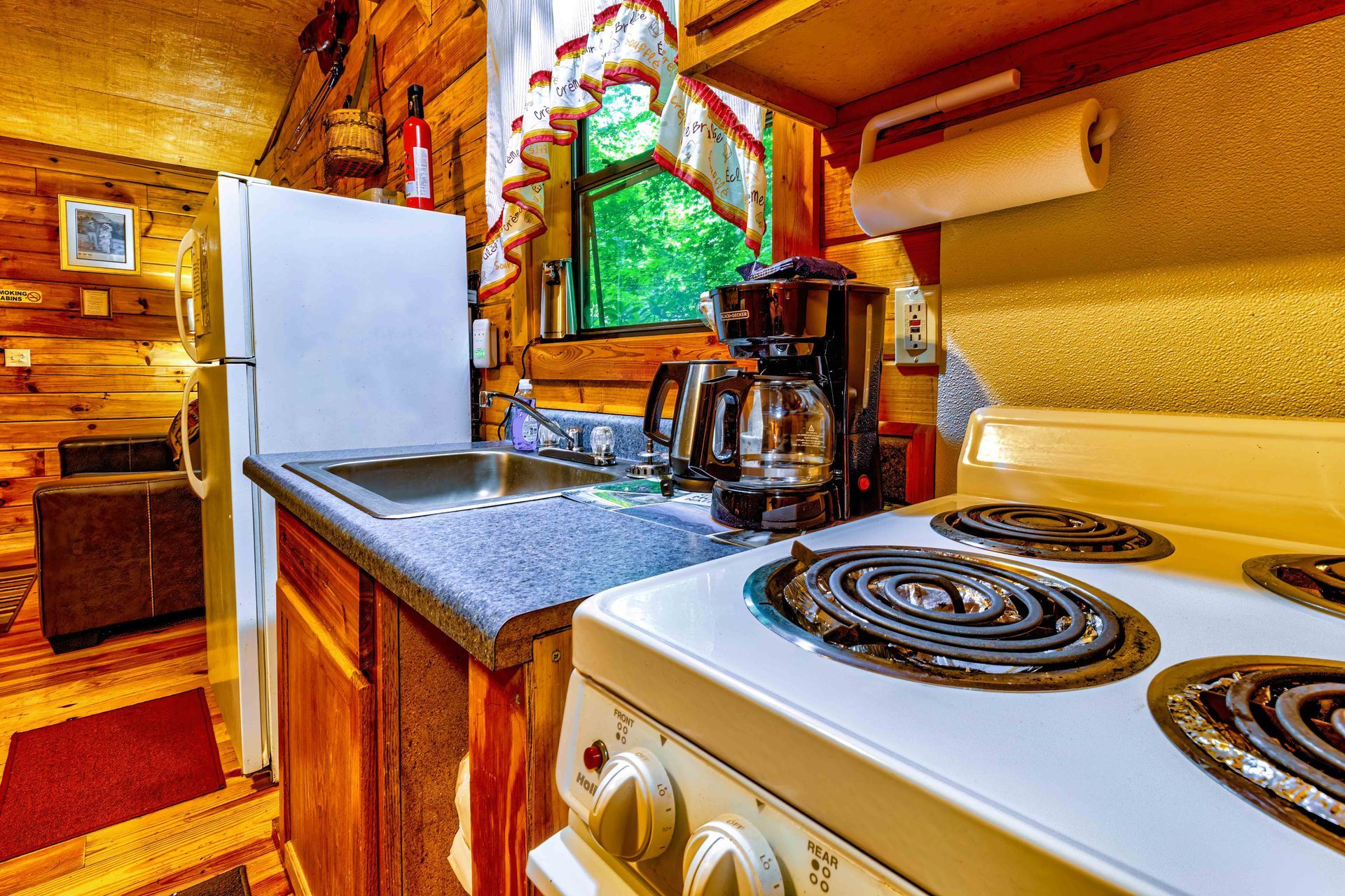 Rustic kitchen with white stove, refrigerator, wood-paneled walls, and a window over the sink