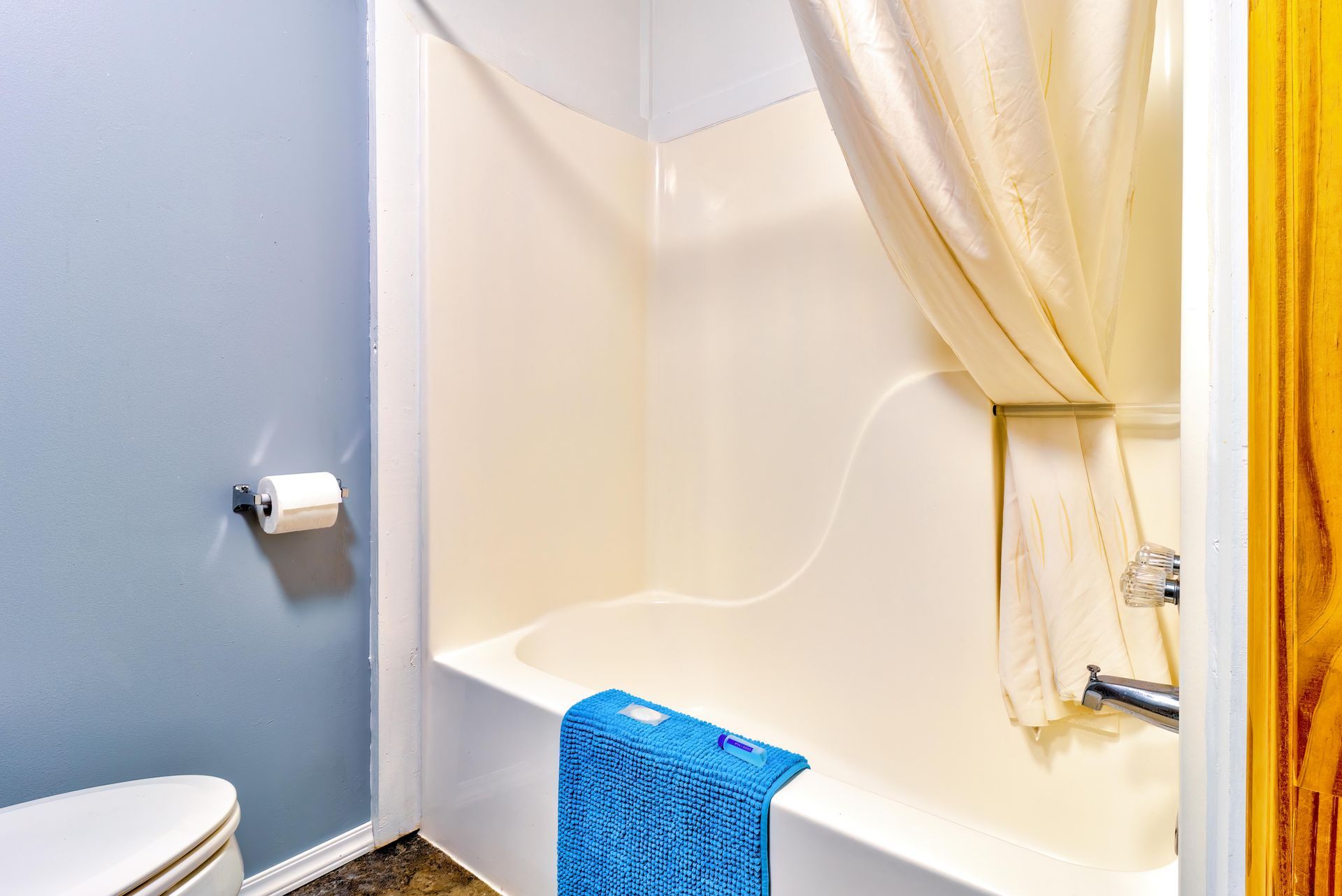 Small bathroom with a white tub, beige shower curtain, blue towel, and blue wall.