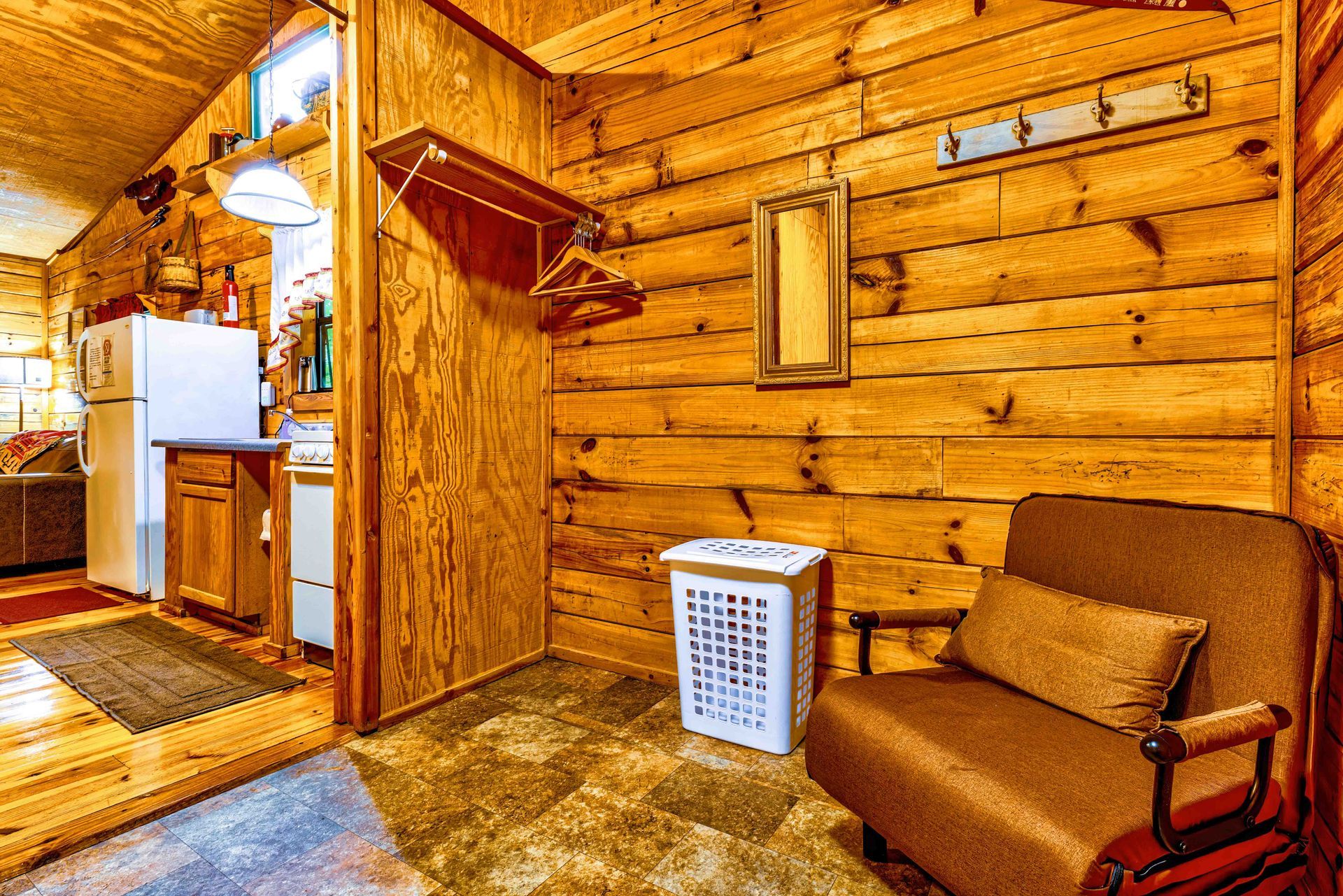 Cozy log cabin interior with wood walls, staircase, laundry basket, and brown chair near an entryway
