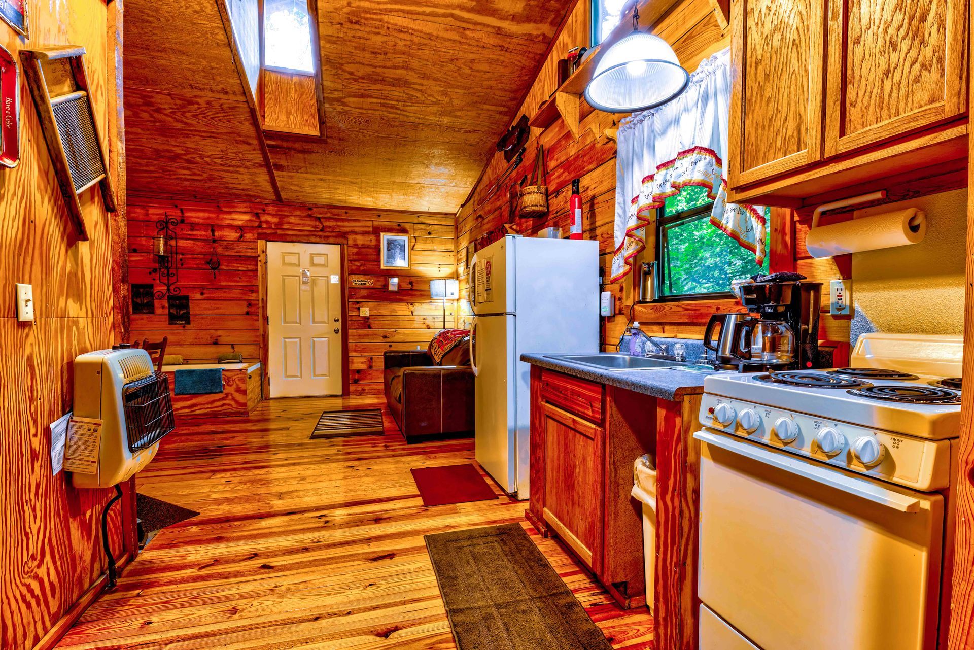 Rustic kitchen interior with wooden cabinets, white stove, refrigerator, and sunlit window view