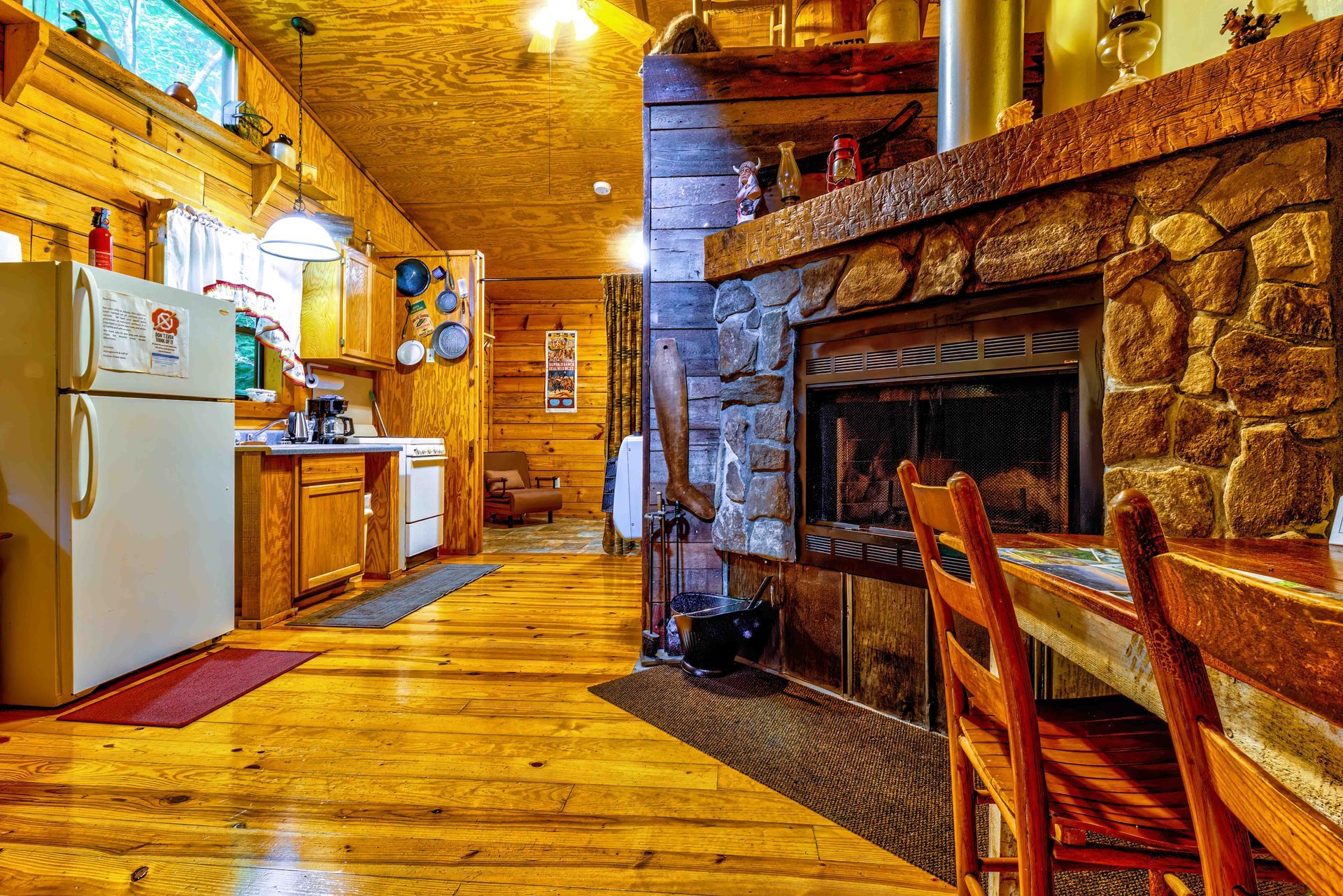 Rustic cabin kitchen with wooden floors, stone fireplace, and warm amber lighting