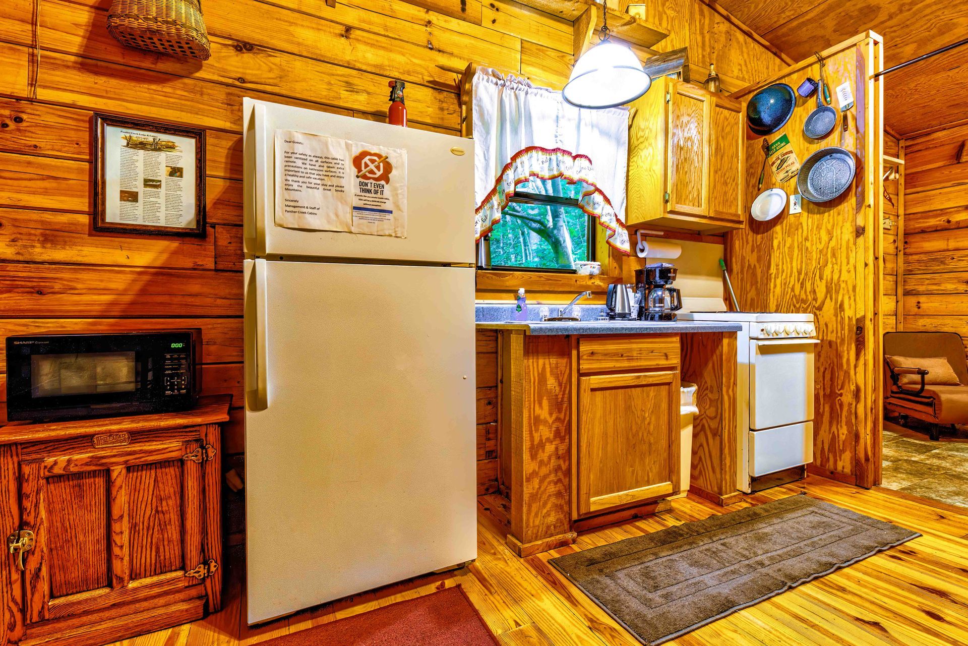 Cozy rustic kitchen with wood walls, refrigerator, cabinets, stove, sink, and hanging pans.