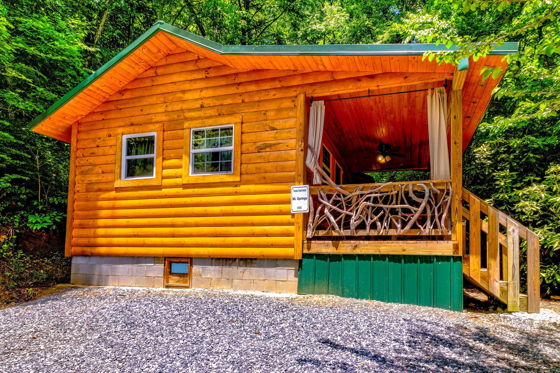 Small orange wooden cabin with a porch and stairs, set on a gravel lot beside green trees.