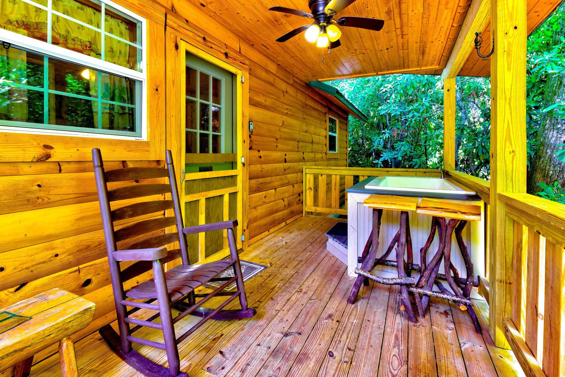 Wooden porch with rocking chair, table, and lush green view beyond the railing