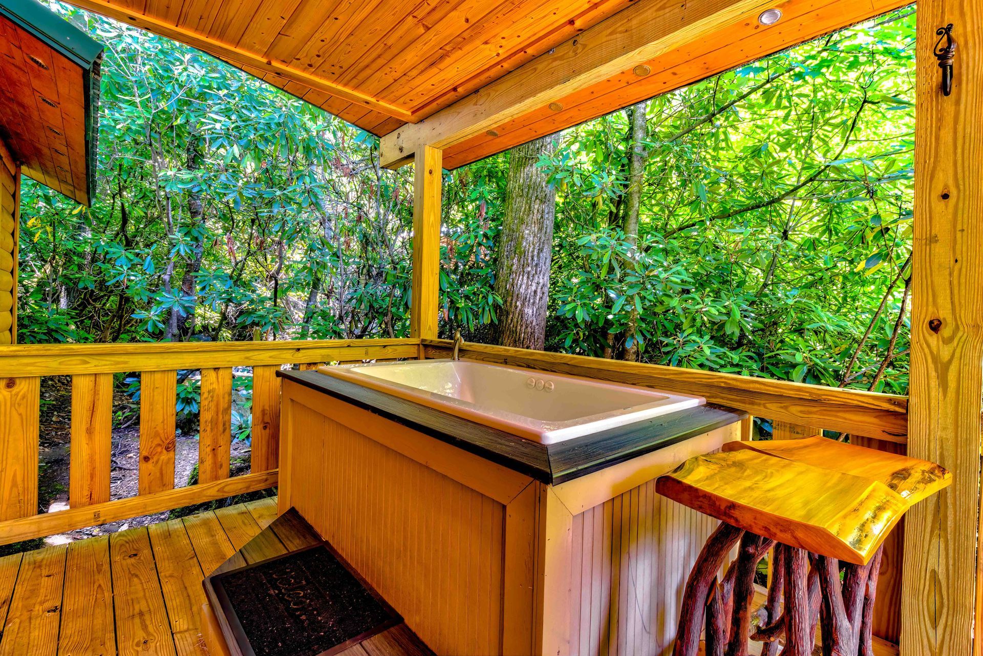 Wooden hot tub on a covered deck surrounded by lush green trees