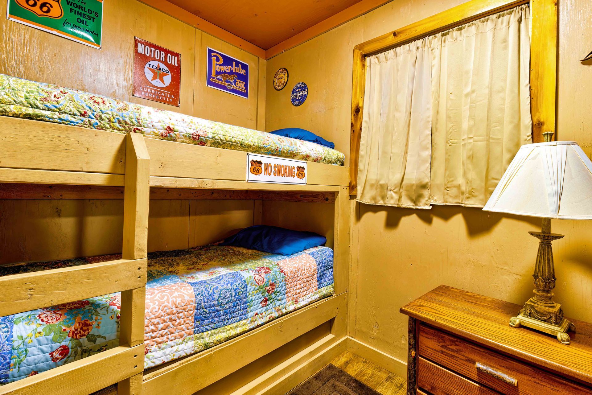 Bunk bed bedroom with colorful quilts, yellow walls, curtained window, and bedside lamp