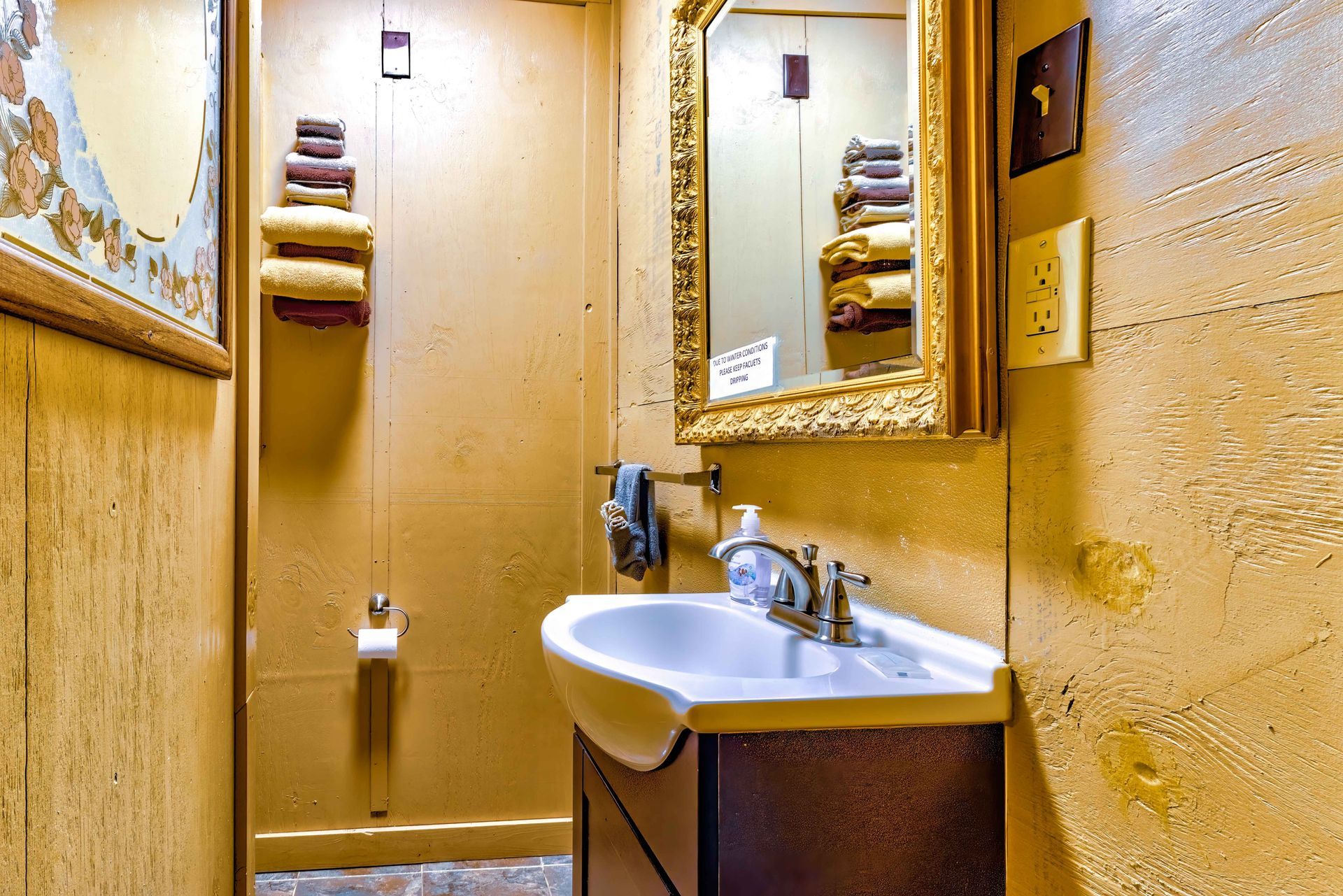 Small narrow bathroom with a sink, mirror, and toilet paper shelves in warm yellow tones