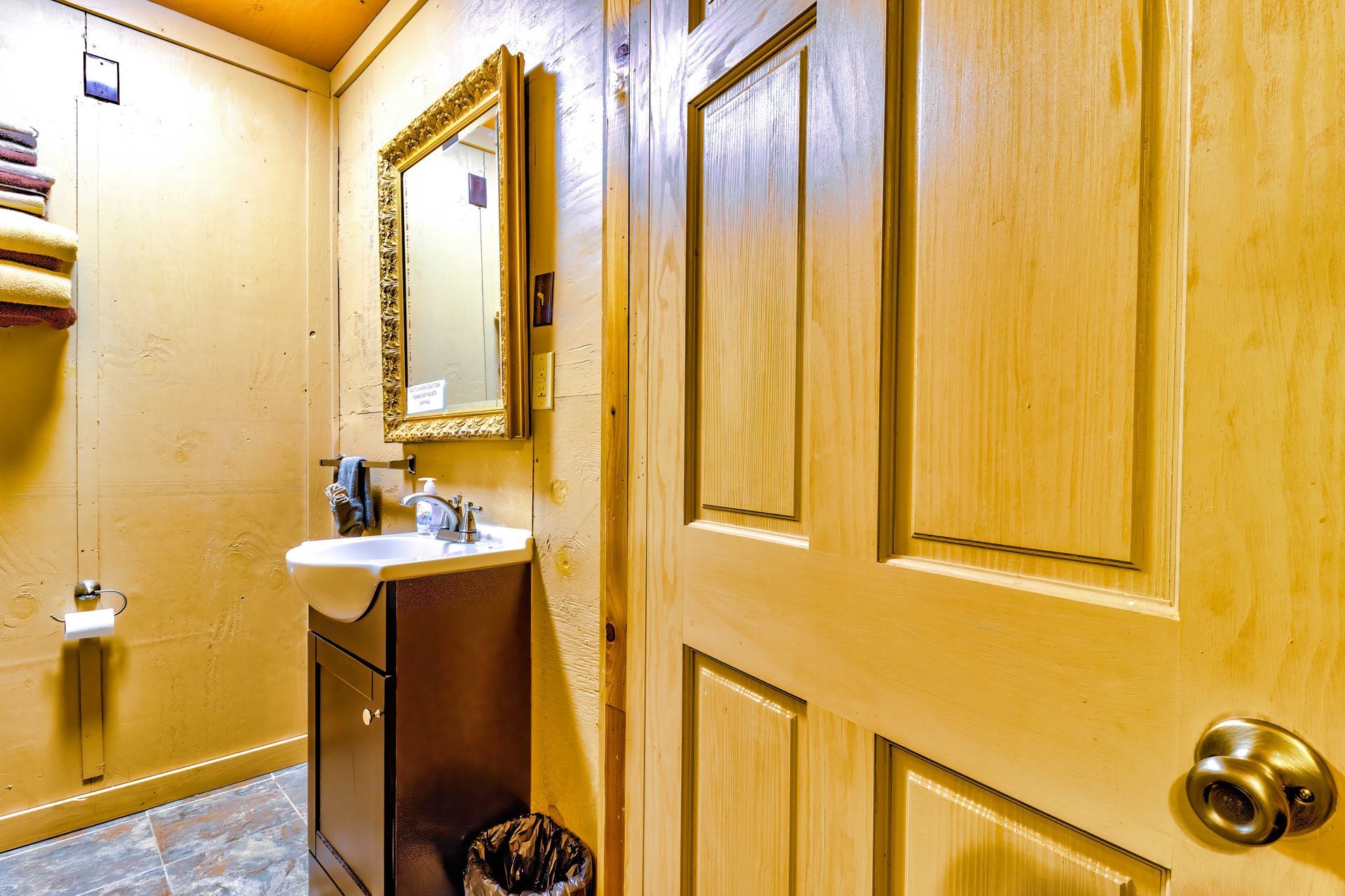 Small bathroom with tan walls, wooden door, mirror, and white sink vanity.